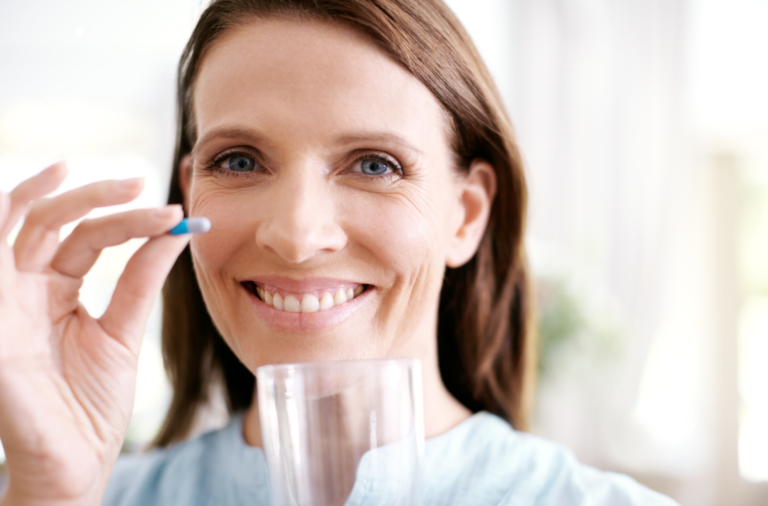 Older woman showing pill in front and about to drink the supplement